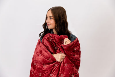Girl wrapped in a red blanket with white snowflakes.