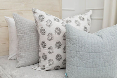 A close up view of a bed made with light gray waffle textured zipper bedding and a white and gray floral printed and light blue pillows.
