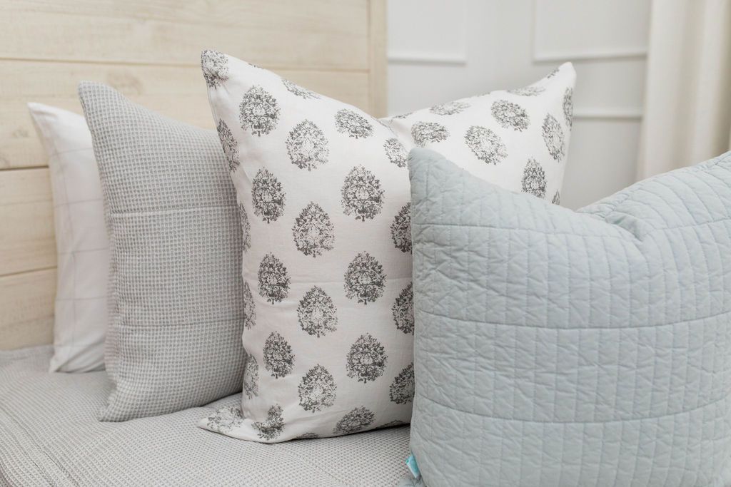 A close up view of a bed made with light gray waffle textured zipper bedding and a white and gray floral printed and light blue pillows.