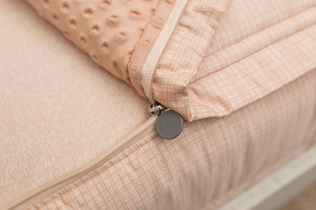 A close up view of a bed made with peach pink zipper bedding with the bed slightly unzipped to reveal the minky comforter and the lighter peach pink bottom cotton lining.