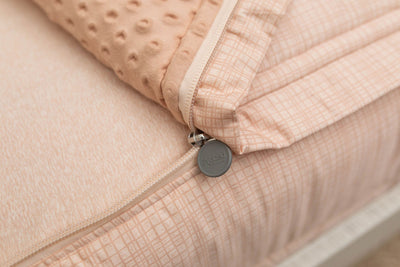A close up view of a bed made with peach pink zipper bedding with the bed slightly unzipped to reveal the minky comforter and the lighter peach pink bottom cotton lining.