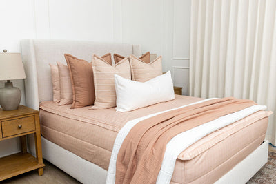 A Queen bed made with peachy pink zipper bedding and an assortment of pink and terra cotta bedding accessories