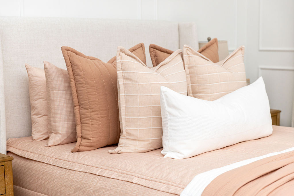 Close up shot of the terra cotta, pink, and white pillows on the bed made with peachy pink zipper bedding