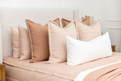 Close up shot of the terra cotta, pink, and white pillows on the bed made with peachy pink zipper bedding