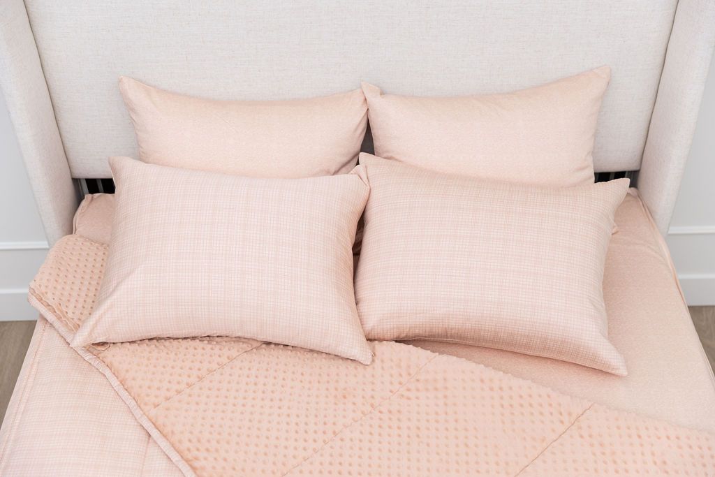 A bed made with peachy pink zipper bedding, the top pulled back to reveal the minky lining, with four pillows laying on top of the bed