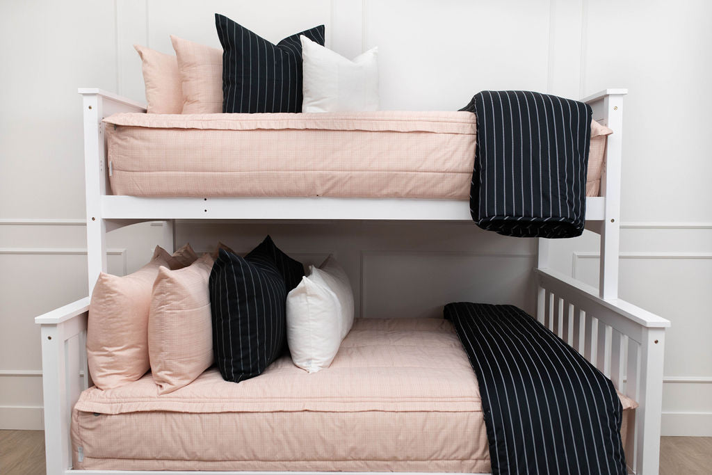 A standard bunk bed with both bunks made with peach pink zipper bedding and neutral and black striped pillows and blankets.