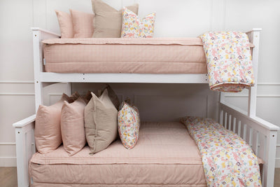 A standard bunk bed with both bunks made with peach pink zipper bedding and neutral and multicolor floral pillows and blankets.