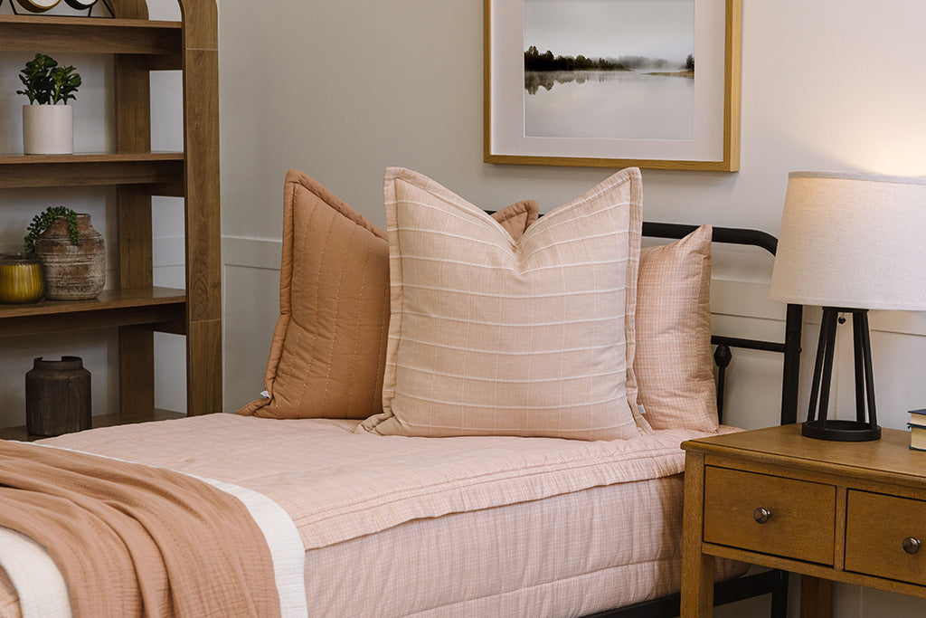 A twin bed made with peach pink zipper bedding and adorned with neutral and multicolor floral pattern pillows and blankets.