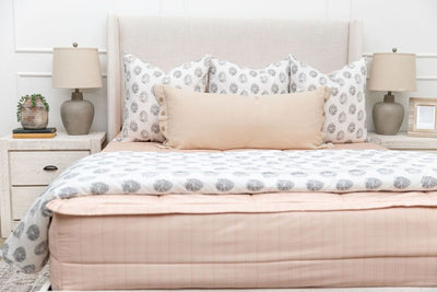 A bed made with peach pink zipper bedding and adorned with gray pattern and neutral pillows and blanket.