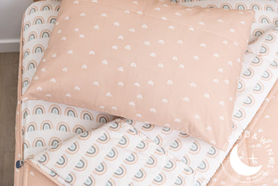 Peachy pink zipper bedding with small white rainbow pattern on the outside unzipped showing pastel rainbow sheet interior