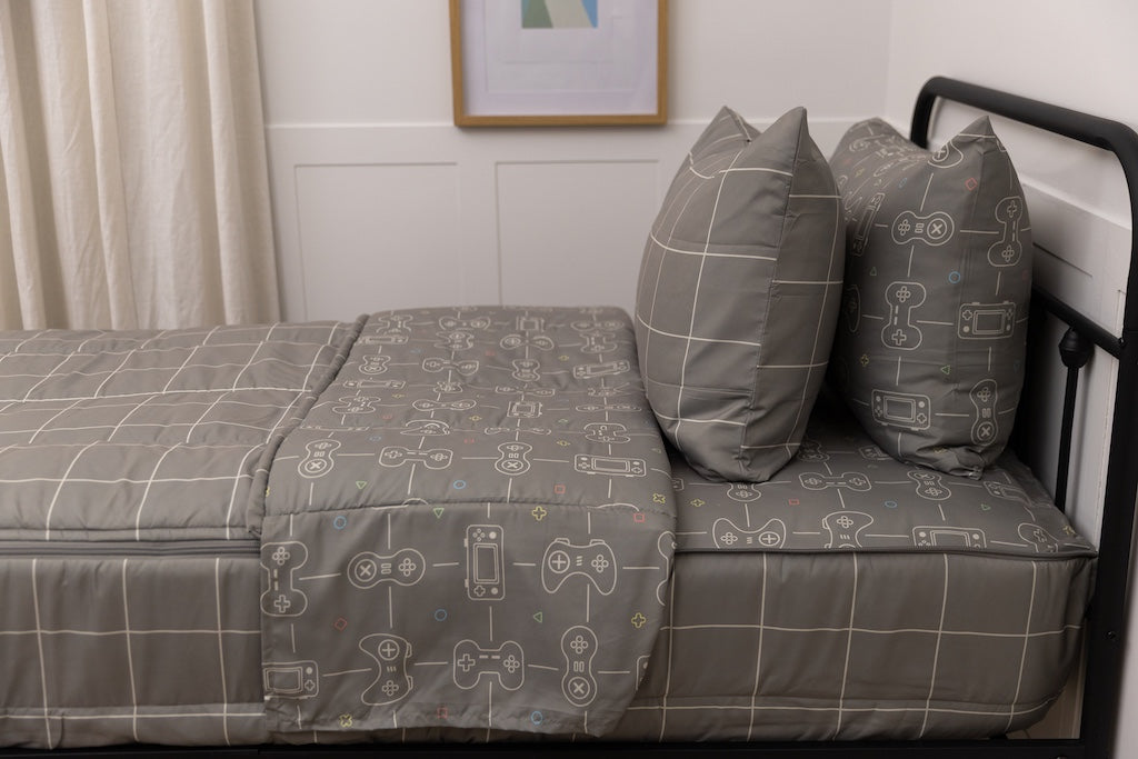 A bed made with gaming printed zipper bedding, showcasing the pillowcase and sham and the top of the bedding turned down to show the inside lining.