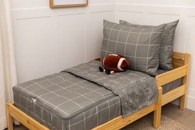 A wooden toddler bed made with gaming printed zipper bedding and a stuffed football leaning against the pillows.