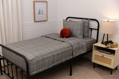 A twin bed made with gaming zipper bedding, a nightstand beside the bed and a stuffed ball propped up against the pillow.