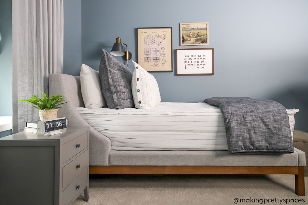 A twin bed made with white and pinstripes zipper bedding and dark charcoal gray pillows and blanket.