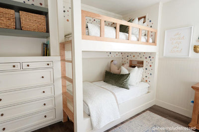 A room with a built in bunk bed with seersucker white zipper bedding on both bunk beds, decorated with neutral and green pillows and blankets.
