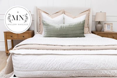 A bed made with seersucker white zipper bedding and an assortment of neutral throw pillows and blankets.