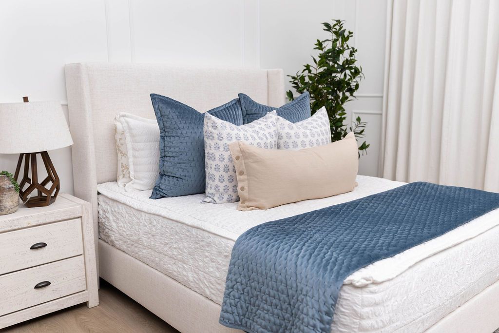 A bed made with seersucker white zipper bedding and an assortment of blue throw pillows and blankets.