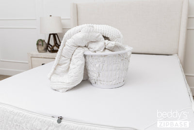 A bed made with just the fitted bedding base around the sides of the mattress, with the top comforter and ZipBase sheet in a basket on top of the bed.