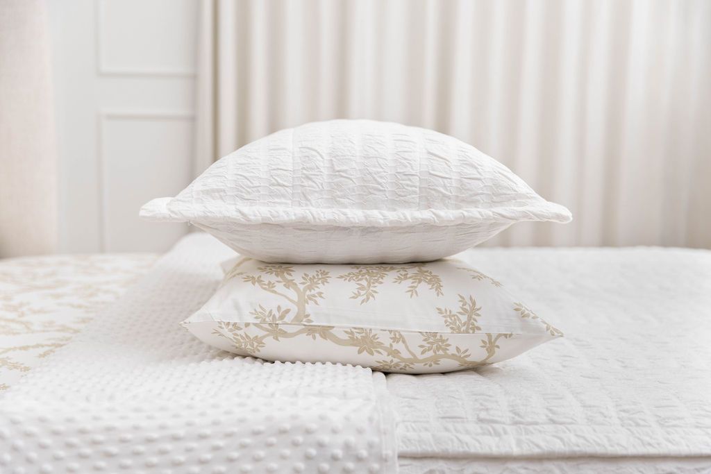 A pillow in a neutral floral pillowcase with a pillow in a white seersucker pillow sham stacked on top, both sitting on a bed made with white seersucker zipper bedding