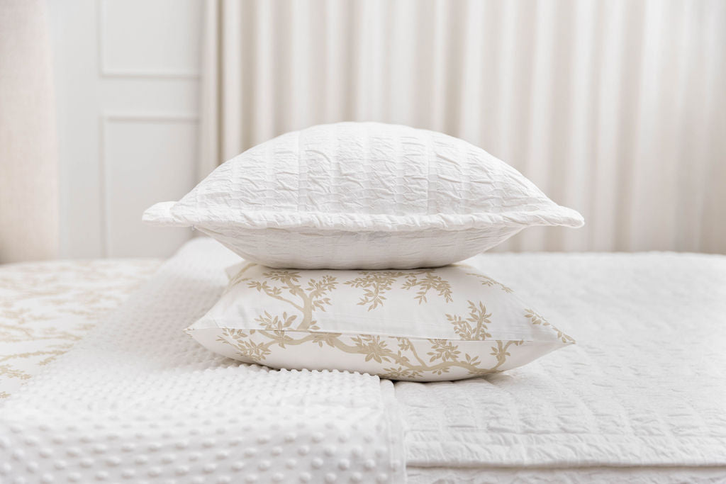 A white seersucker sham stacked on top of a neutral floral pillowcase, on top of a bed made with white seersucker zipper bedding.