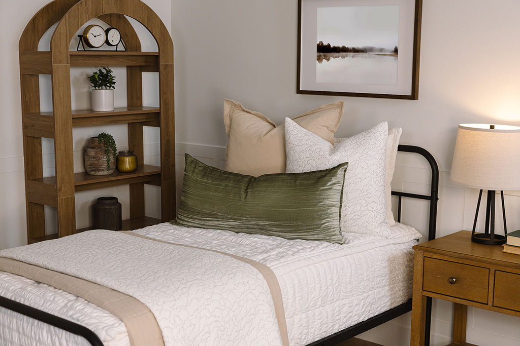 A twin bed made with white seersucker zipper bedding and neutral throw pillows and blankets