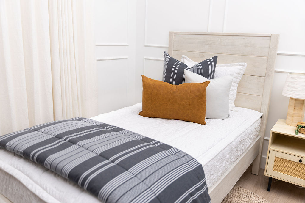 A twin bed made with seersucker white zipper bedding and gray striped pillows and blanket.