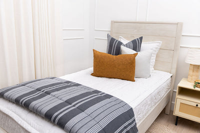 A twin bed made with seersucker white zipper bedding and gray striped pillows and blanket.