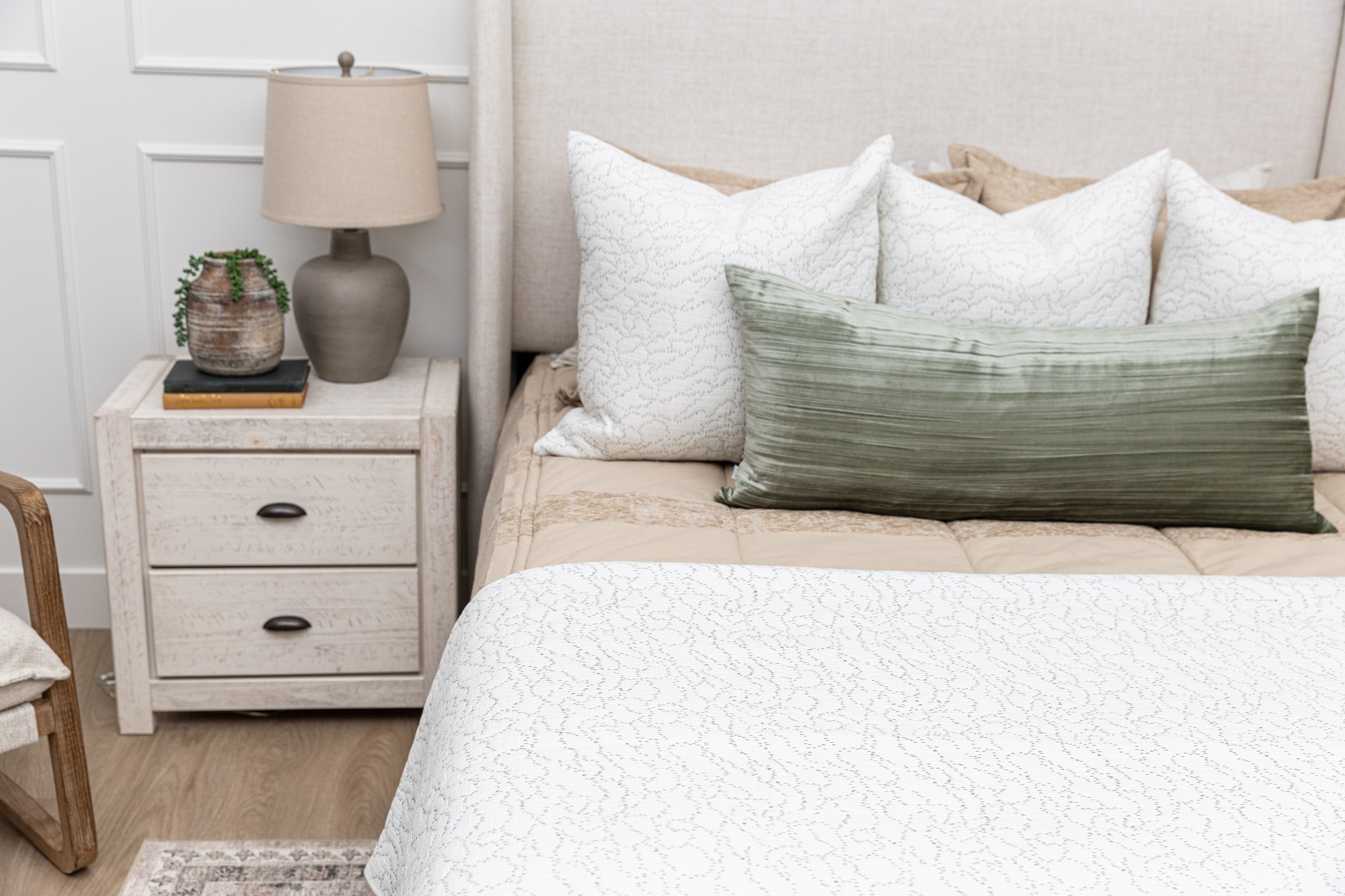 A bed made with tan zipper bedding and an assortment of white and green velvet pillows and blankets.
