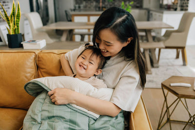 Mother and daughter laughing and cuddling on couch with a green dotted stripe children's blanket