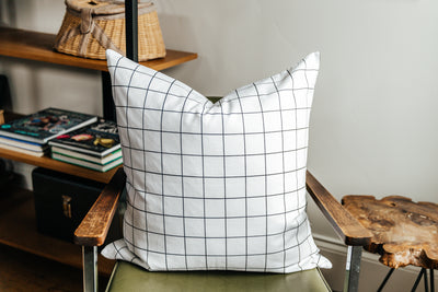 A white euro pillow with a black grid pattern arranged on a green metal chair.
