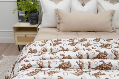 A close up of a bed made with tan striped zipper bedding and neutral pillows with a western cowboy printed blanket.