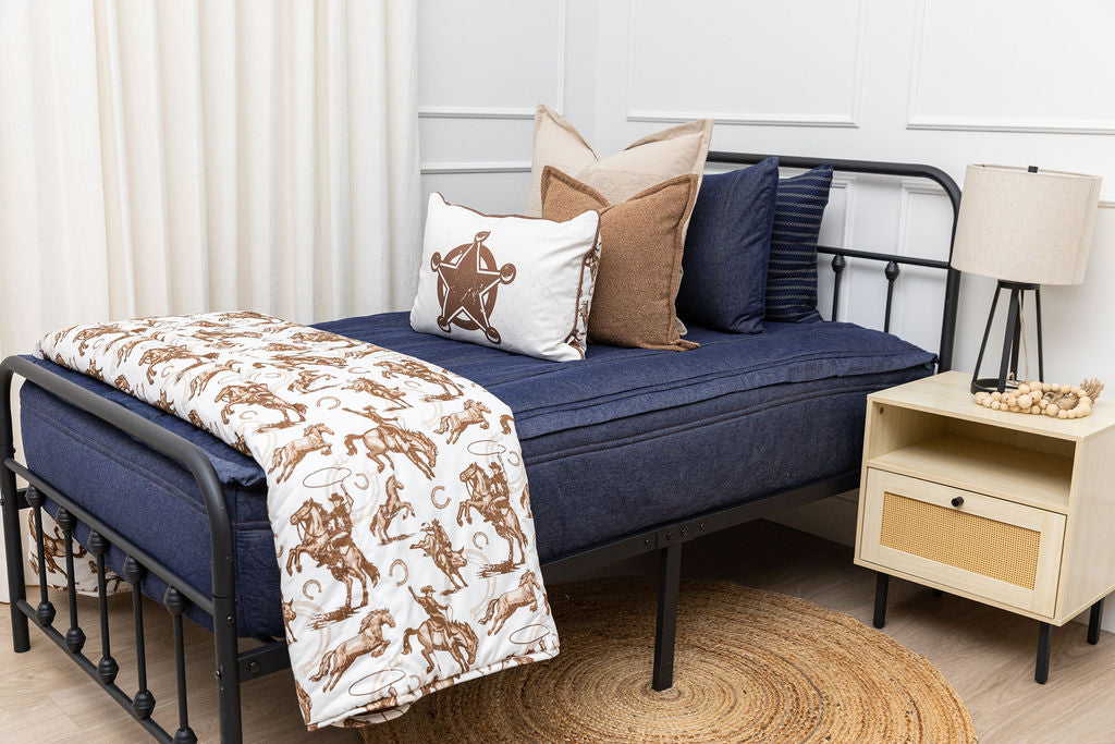A twin bed made with dark denim blue zipper bedding and an assortment of neutral pillows and a cowboy western printed blanket.