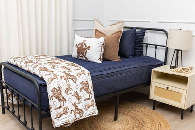 A twin bed made with dark denim blue zipper bedding and an assortment of neutral pillows and a cowboy western printed blanket.