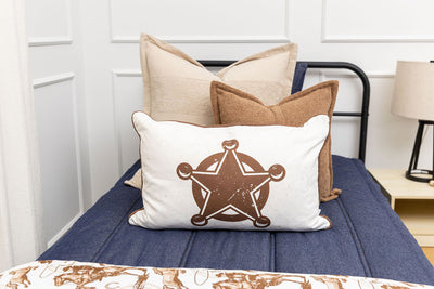 A close up of a twin bed made with dark denim blue zipper bedding and an assortment of neutral pillows and a cowboy western printed blanket.