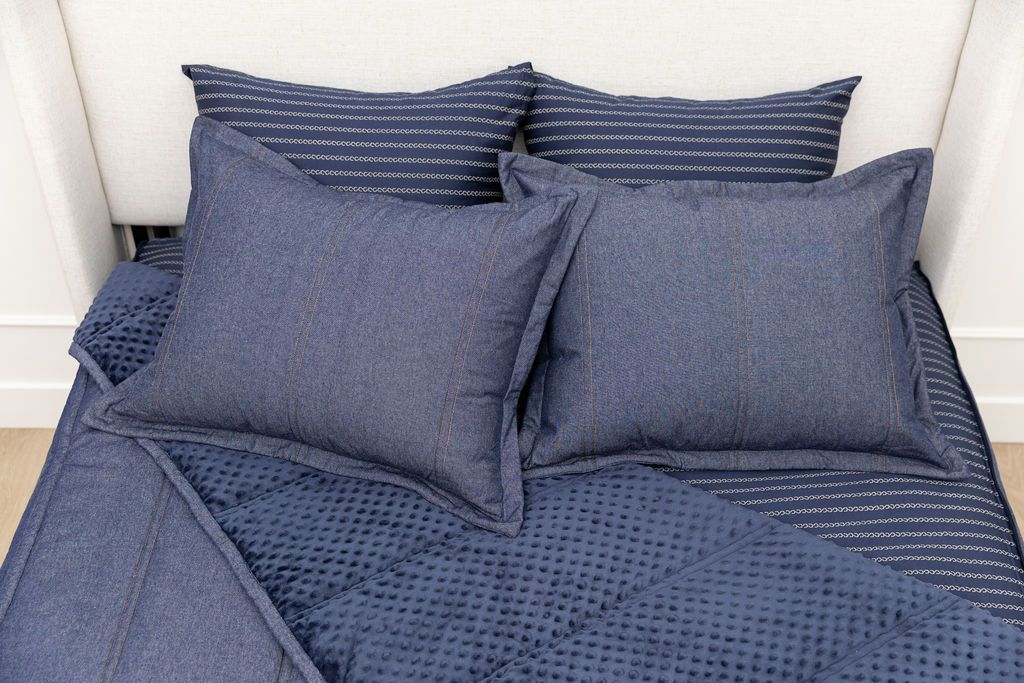 A bed made with dark denim blue zipper bedding with the comforter pulled back and pillows on top of the bed.