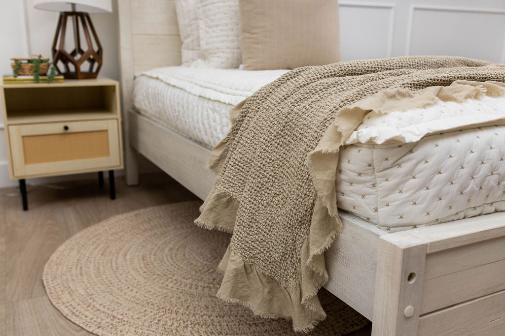A side view of a bed made with cream embroidered zipper bedding with a tan waffle textured throw blanket folded over the end of the bed.