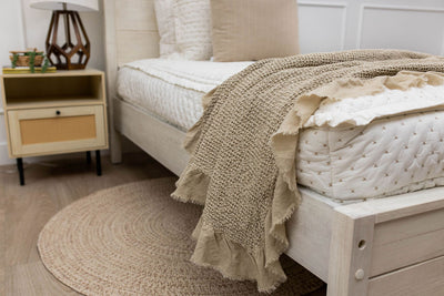 A side view of a bed made with cream embroidered zipper bedding with a tan waffle textured throw blanket folded over the end of the bed.