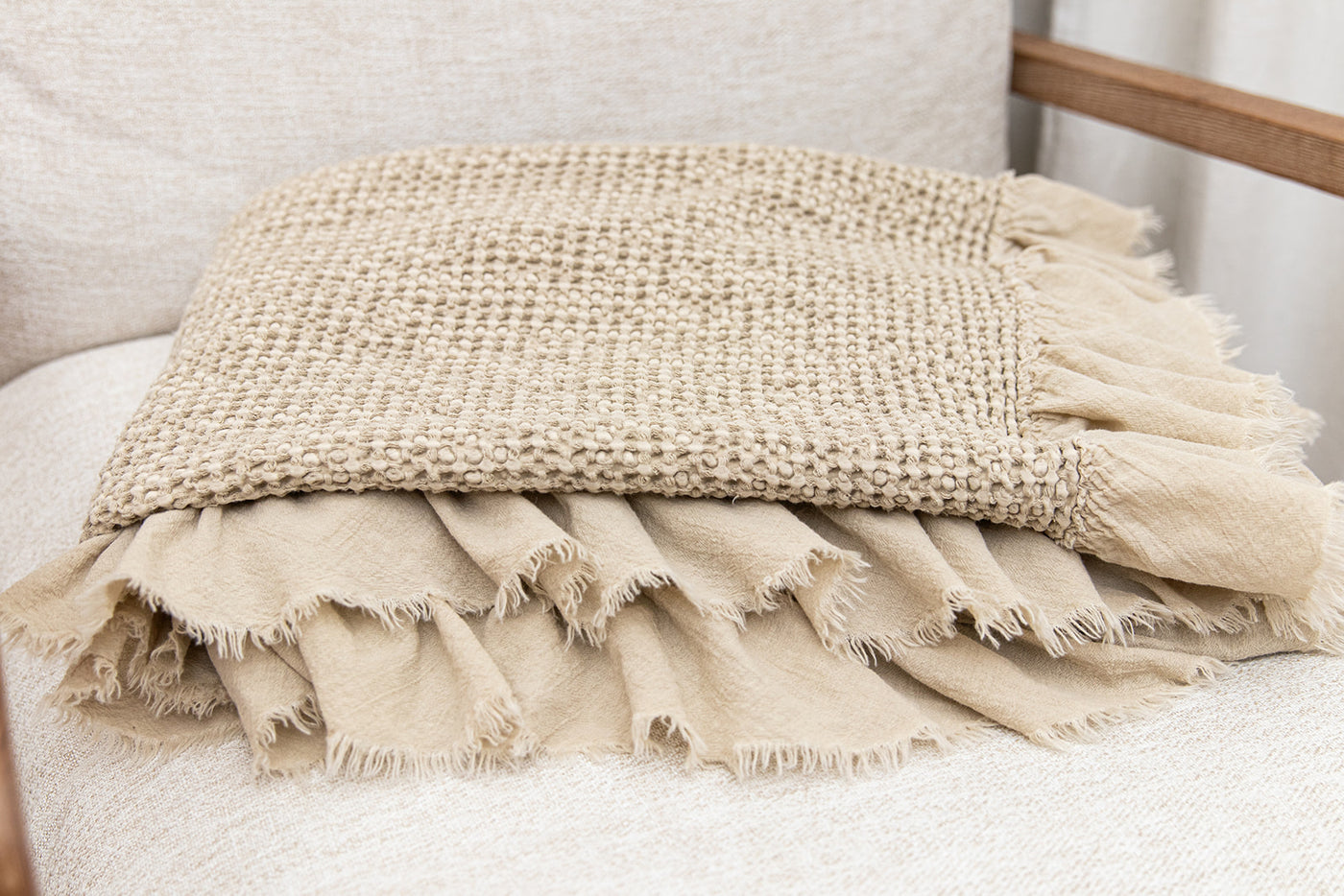 A close up of a tan waffle textured throw blanket folded on a chair seat.