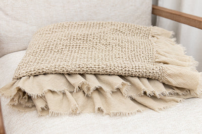 A close up of a tan waffle textured throw blanket folded on a chair seat.