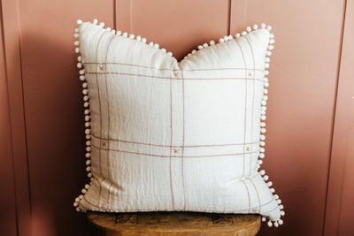 White Pillow on stool with pink grid pattern and pom pom outline