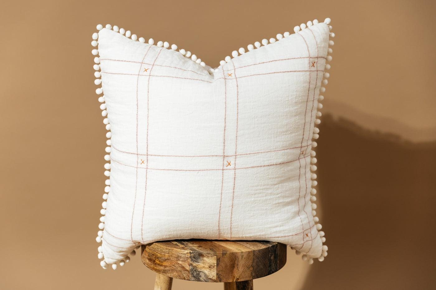White Pillow on stool with grid pattern and pom pom edges