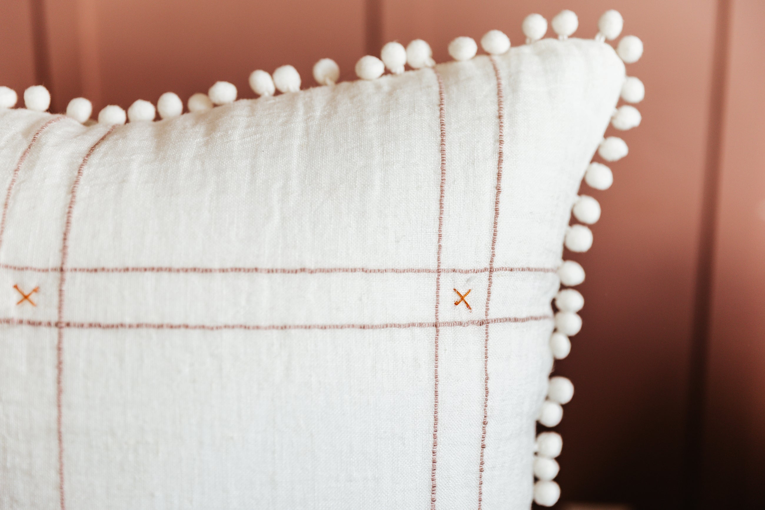 A close up view of a white pillow with a grid pattern and pom pom edges