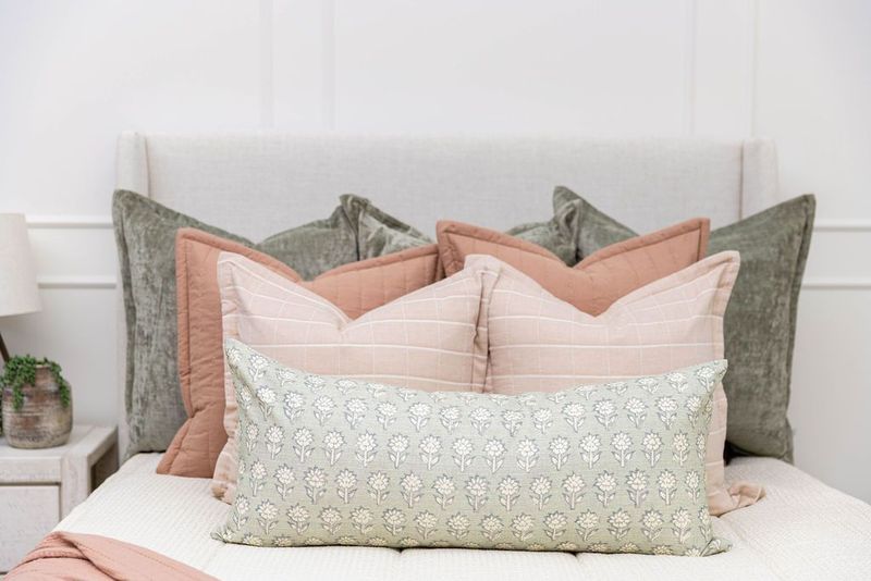 A close up of an assortment of pink, terra cotta, and green throw pillows arranged on a bed made with cream waffle zipper bedding.