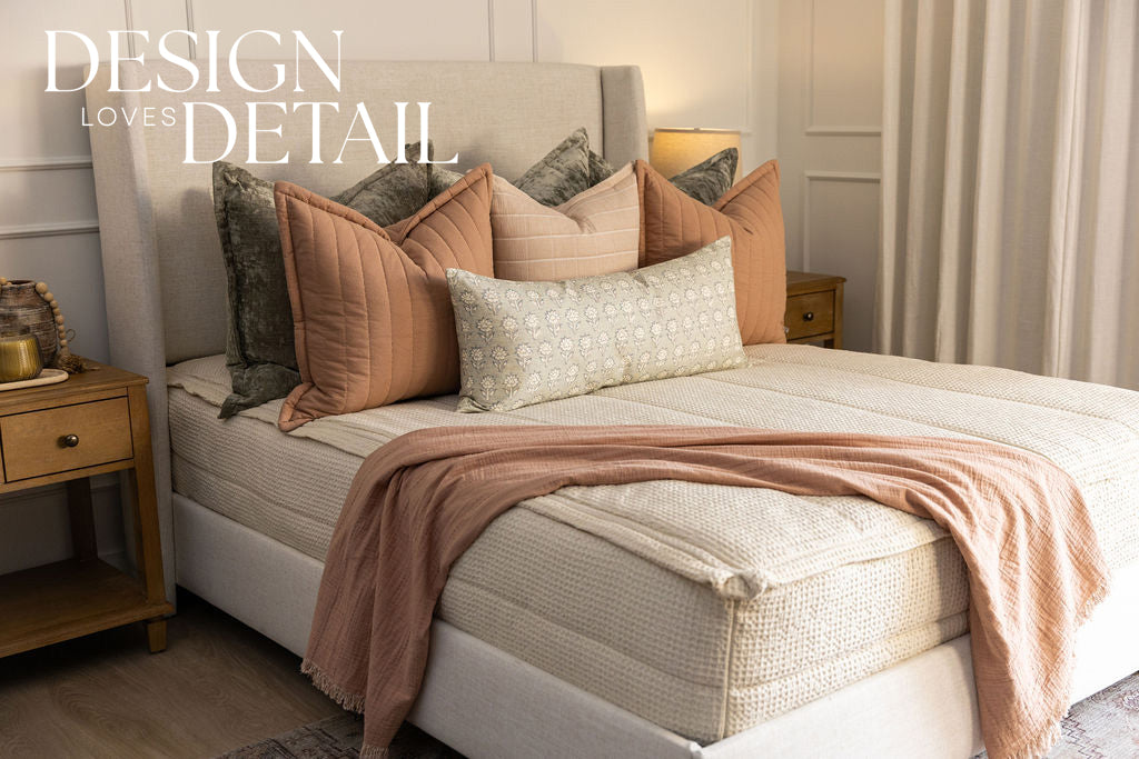 A queen bed made with cream waffle zipper bedding and an assortment of pink and green pillows, all designed by Design Loves Detail