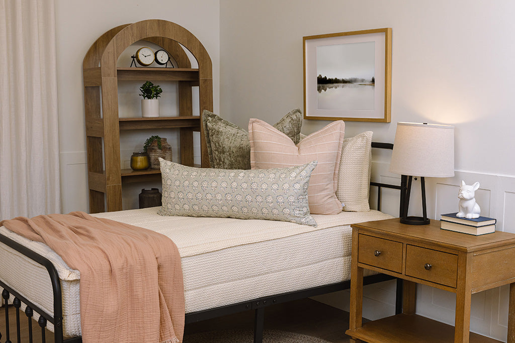 A close up of an assortment of pink, terra cotta, and green throw pillows arranged on a bed made with cream waffle zipper bedding.