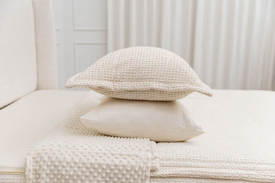 A cream pillowcase and matching sham on a made bed with cream waffle textured zipper bedding. 