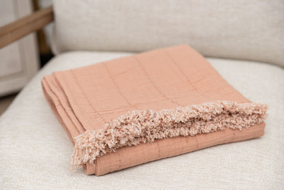 A terra cotta pin throw blanket folded up sitting on a chair