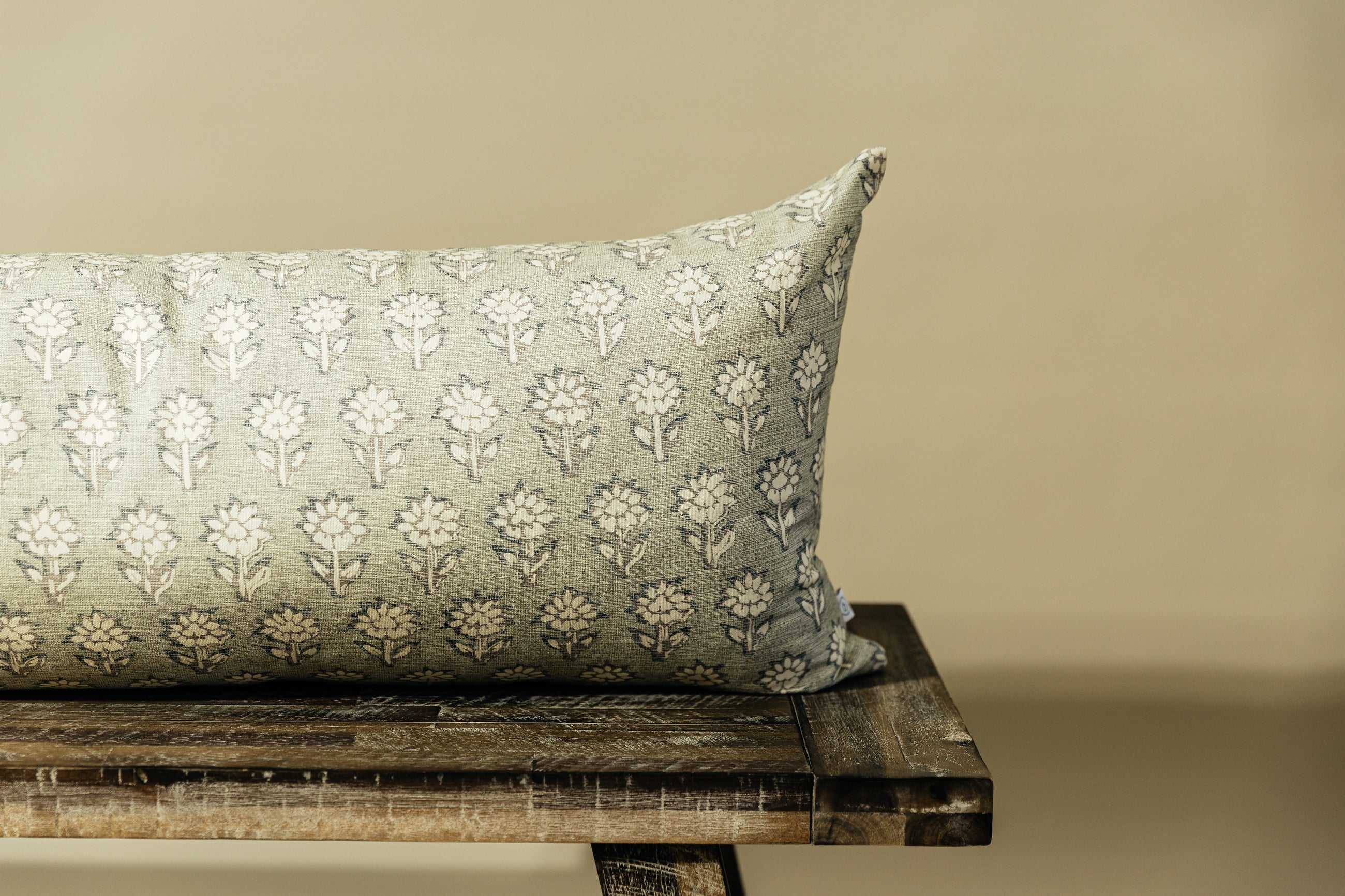 A partial close up view of a sage green and blue floral pattern XL lumbar pillow arranged on a bench with a light green background.