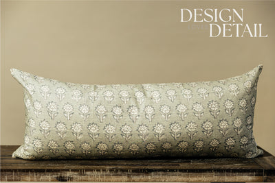 A sage green and blue floral pattern XL lumbar pillow arranged on a bench with a light green background.