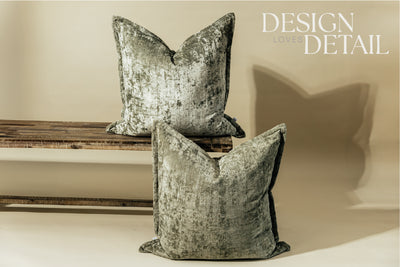 Two sage velvet green XL euro pillows on a bench and on the ground while arranged on a light green background.